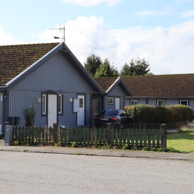 Blåa trähus med vita dörrar på Lovisagatan i Höör, gräsplan och grönmålat staket utanför.