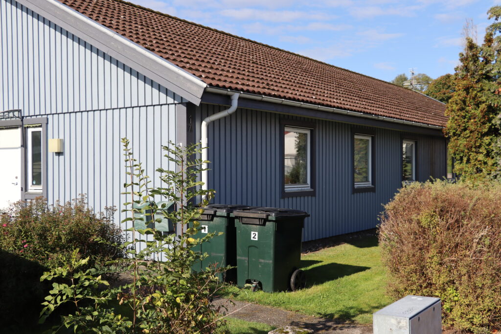 Blått hus trä från sidan med tre fönster och gräsmatta utanför.