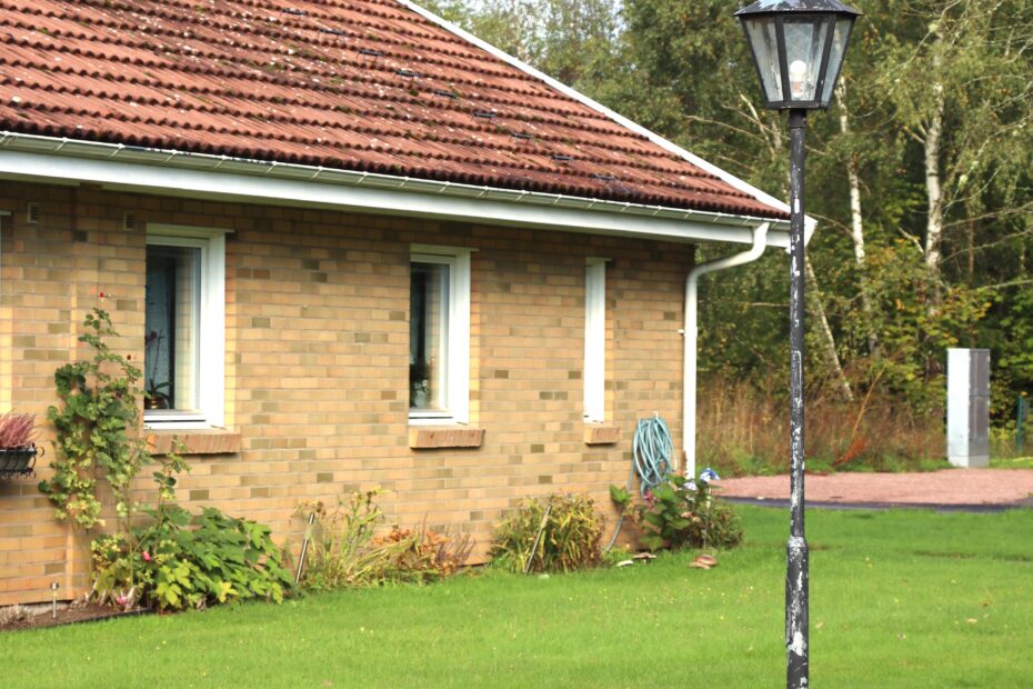 Husknut med ljusbrunt tegel, vita fönster och lyktstolpe på gräsmattan utanför.