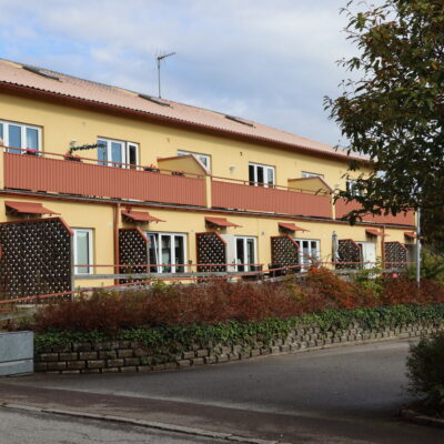 Gul fastighet på Möllebacken 3 i Höör, hyresrätterna är separerade med röd balkong och vägg/insynsskydd.