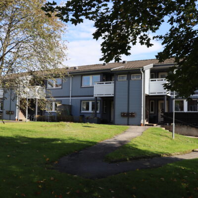 Ljusblått trähus i två våningar med vita balkonger och stor gräsmatta framför fastigheten.