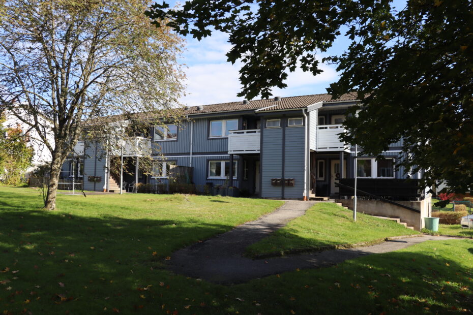 Ljusblått trähus i två våningar med vita balkonger och stor gräsmatta framför fastigheten.